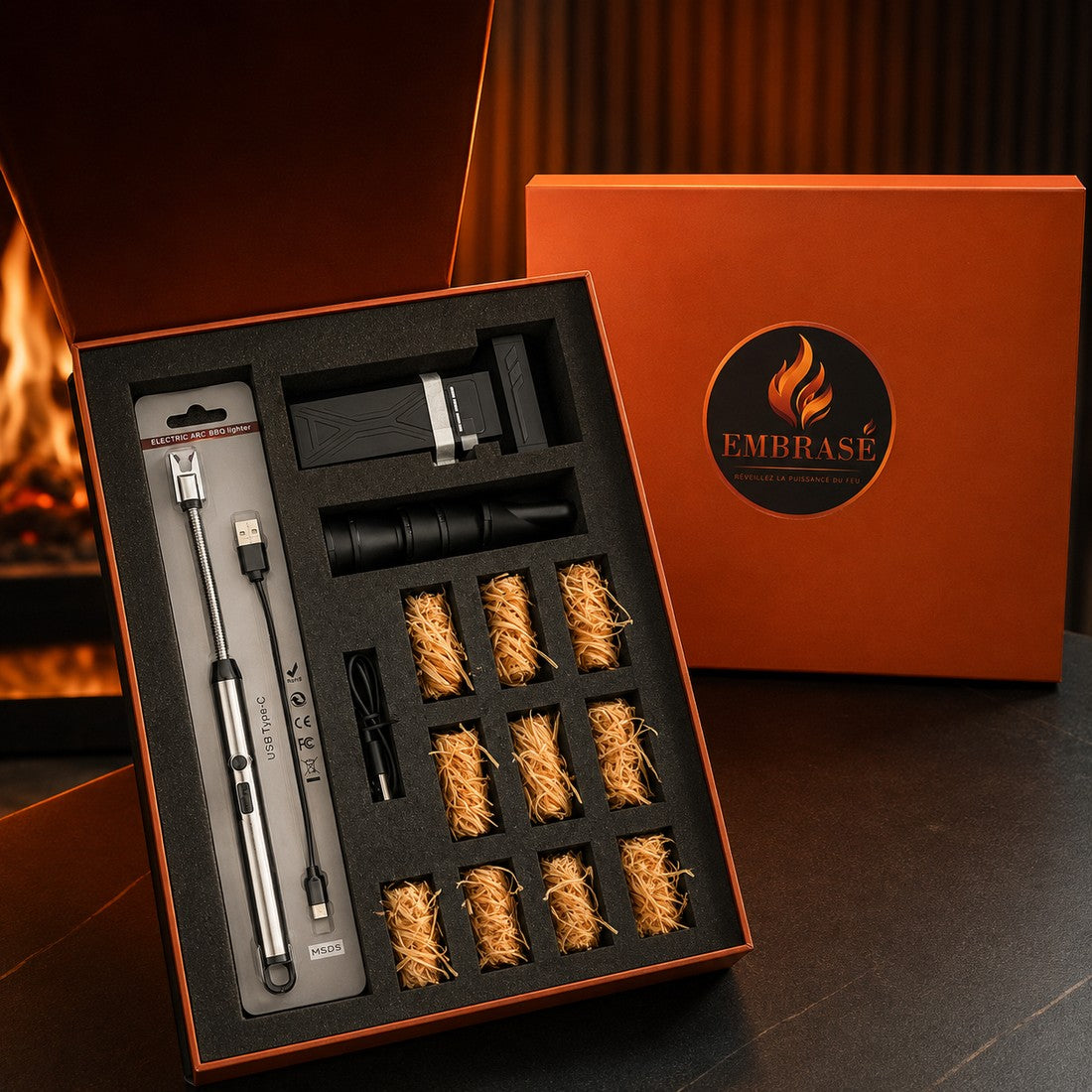 Coffret Signature Embrasé ouvert : souffleur turbo, briquet arc électrique et allume-feux naturels cirés, devant une cheminée